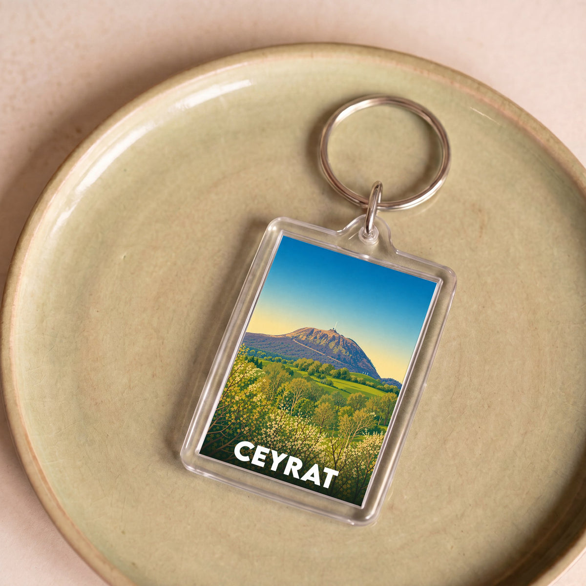 Porte-clés souvenir de la ville de Ceyrat avec une illustration stylisée d'un paysage montagneux.