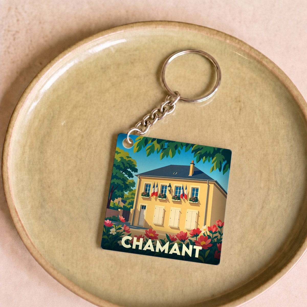 Porte-clés souvenir de la ville de Chamant avec une illustration stylisée d'une maison fleurie.