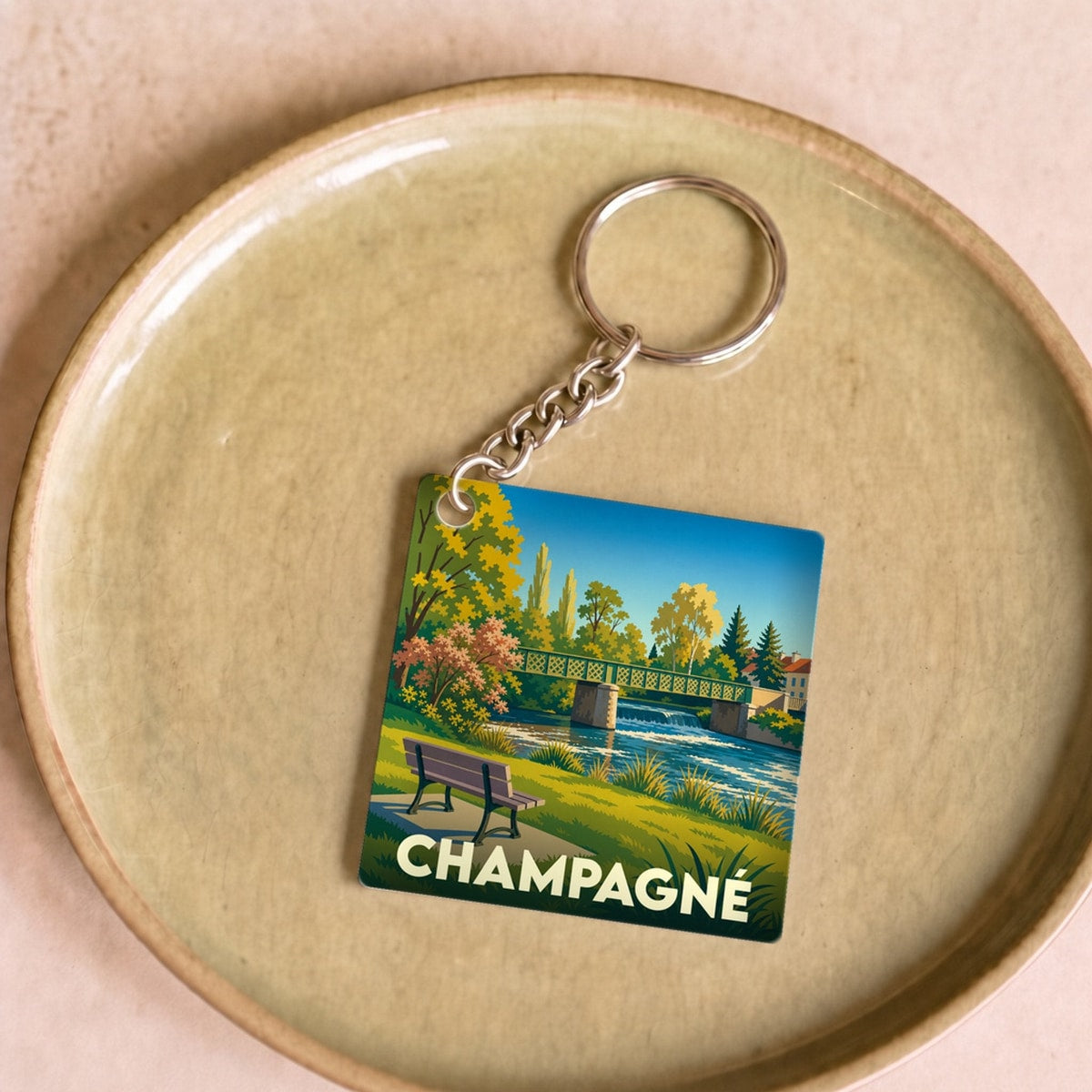 Porte-clés souvenir de la ville de Champagné avec une illustration stylisée d'un paysage de bord de rivière.
