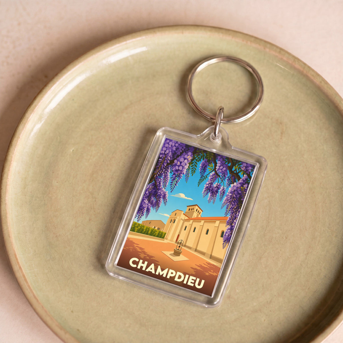 Porte-clés souvenir de la ville de Champdieu avec une illustration stylisée de son prieuré encadré de glycines.