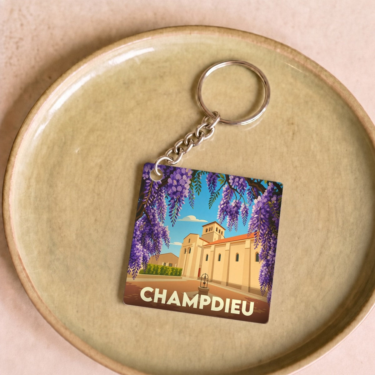 Porte-clés souvenir de la ville de Champdieu avec une illustration stylisée de son prieuré encadré de glycines.