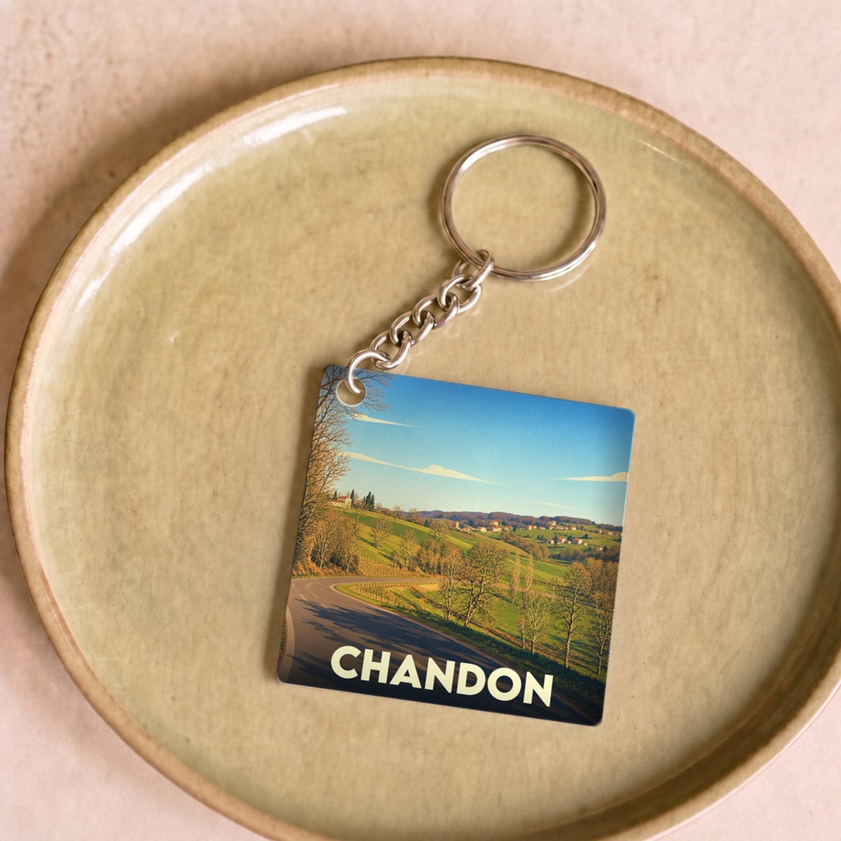 Porte-clés souvenir de la ville de Chandon illustré d'un paysage de campagne ensoleillé.