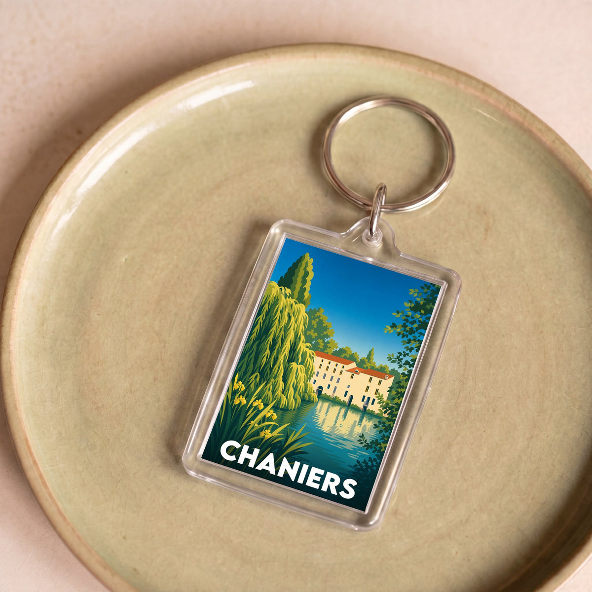 Porte-clés souvenir de la ville de Chaniers avec une illustration stylisée d'un bâtiment au bord de l'eau.
