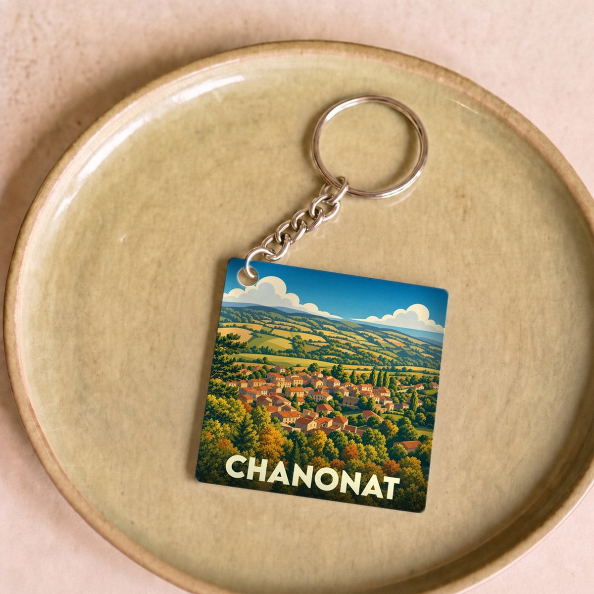Porte-clés souvenir de la ville de Chanonat avec une illustration stylisée de son paysage vallonné.