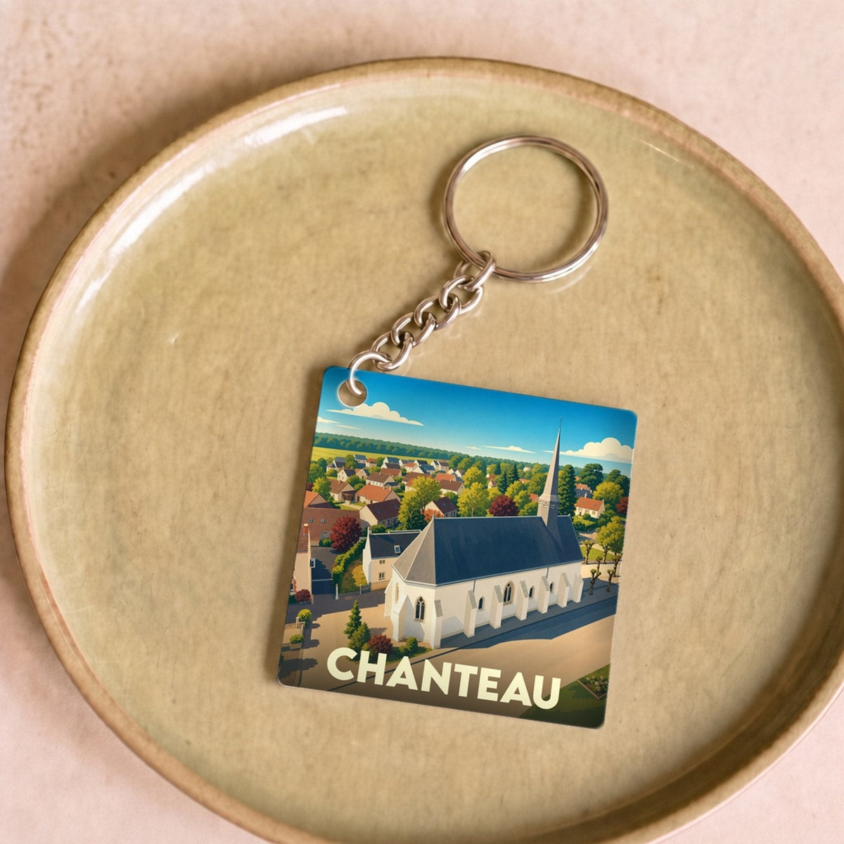 Porte-clés souvenir de la ville de Chanteau avec une illustration stylisée d'une église de campagne.