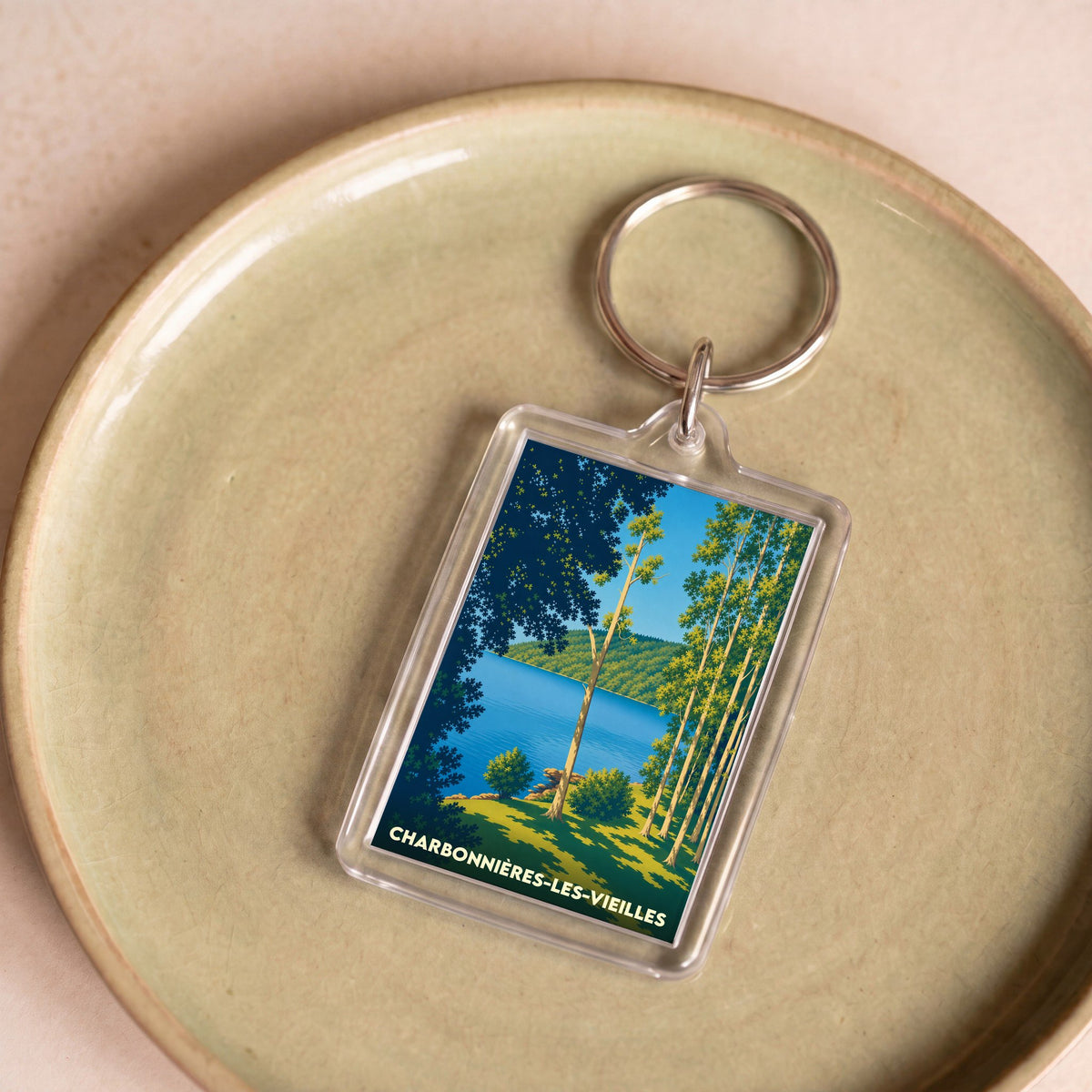 Porte-clés souvenir de la ville de Charbonnières-les-Vieilles avec une illustration stylisée d'un lac bordé d'arbres.