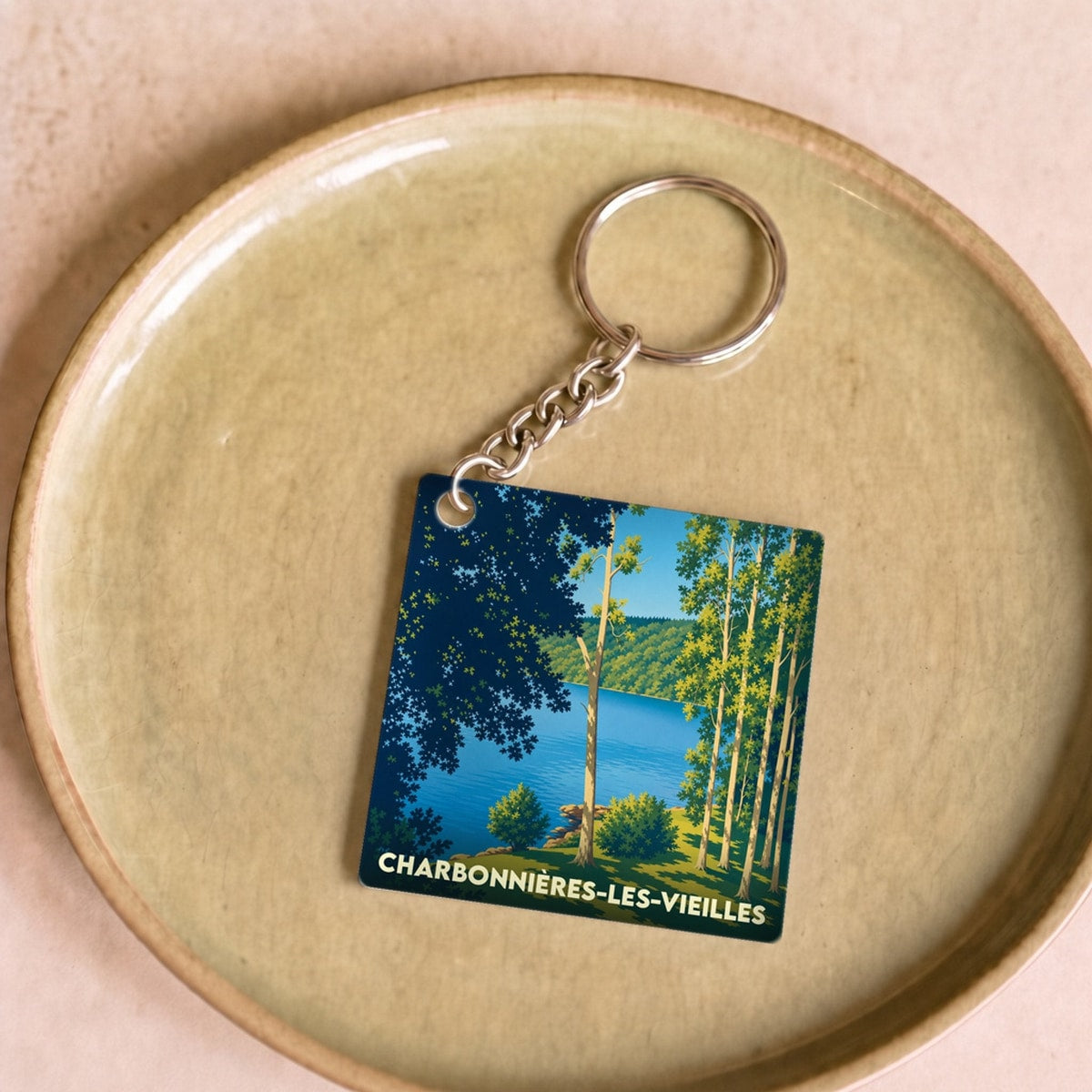 Porte-clés souvenir de la ville de Charbonnières-les-Vieilles avec une illustration stylisée d'un lac bordé d'arbres.