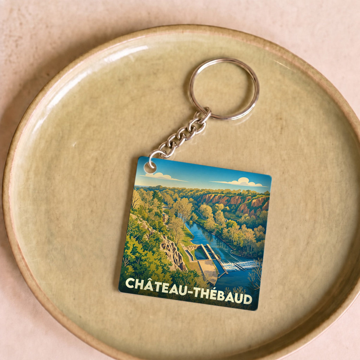 Porte-clés souvenir de la ville de Château-Thébaud avec une illustration stylisée d'un paysage de rivière.