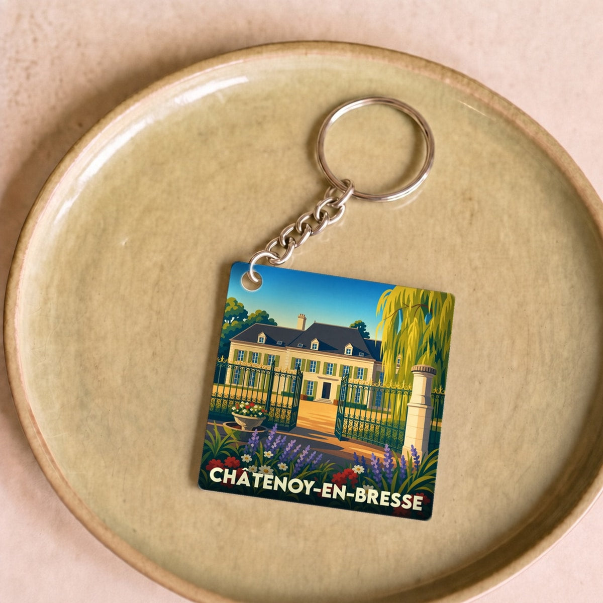 Porte-clés souvenir de la ville de Châtenoy-en-Bresse avec une illustration stylisée d'une demeure bourguignonne et son jardin fleuri.