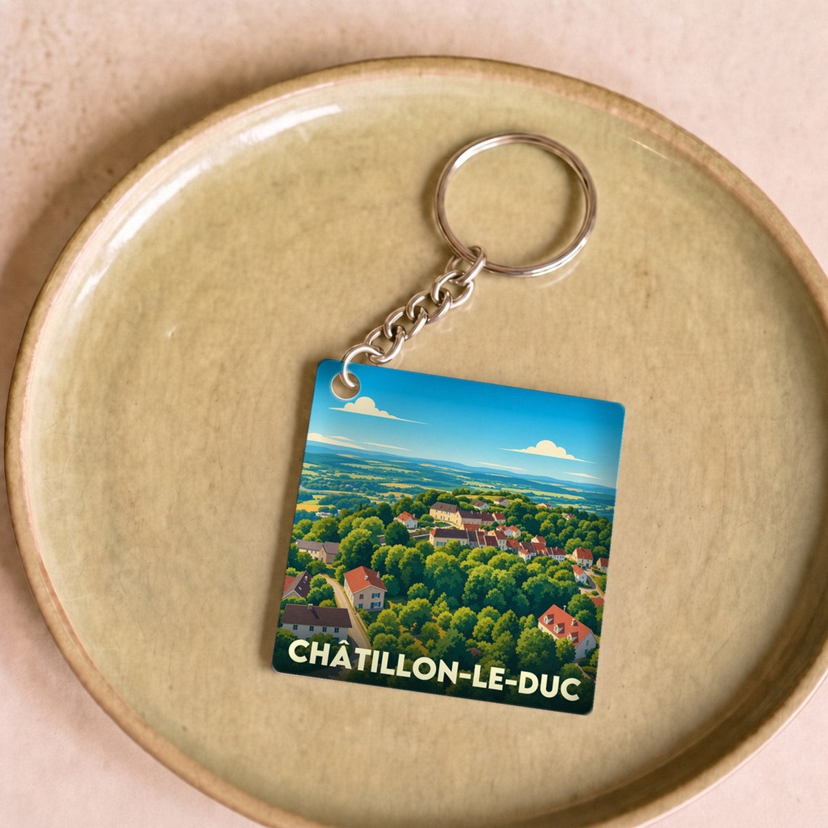 Porte-clés souvenir de la ville de Châtillon-le-Duc avec une illustration stylisée d'un paysage verdoyant.