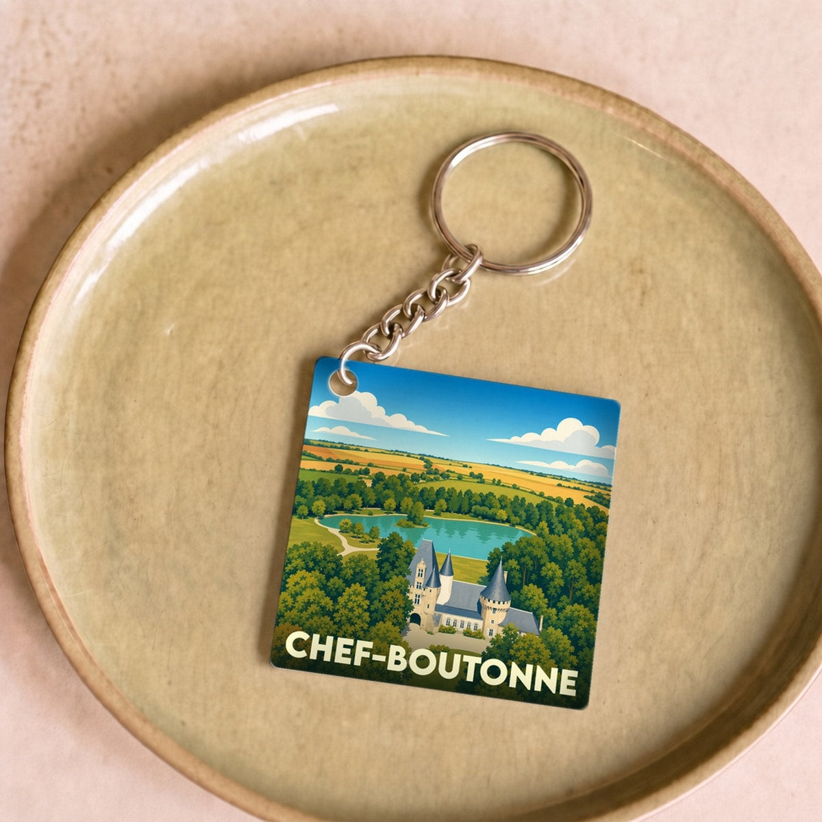 Porte-clés souvenir de la ville de Chef-Boutonne avec une illustration stylisée d'un château entouré de nature.