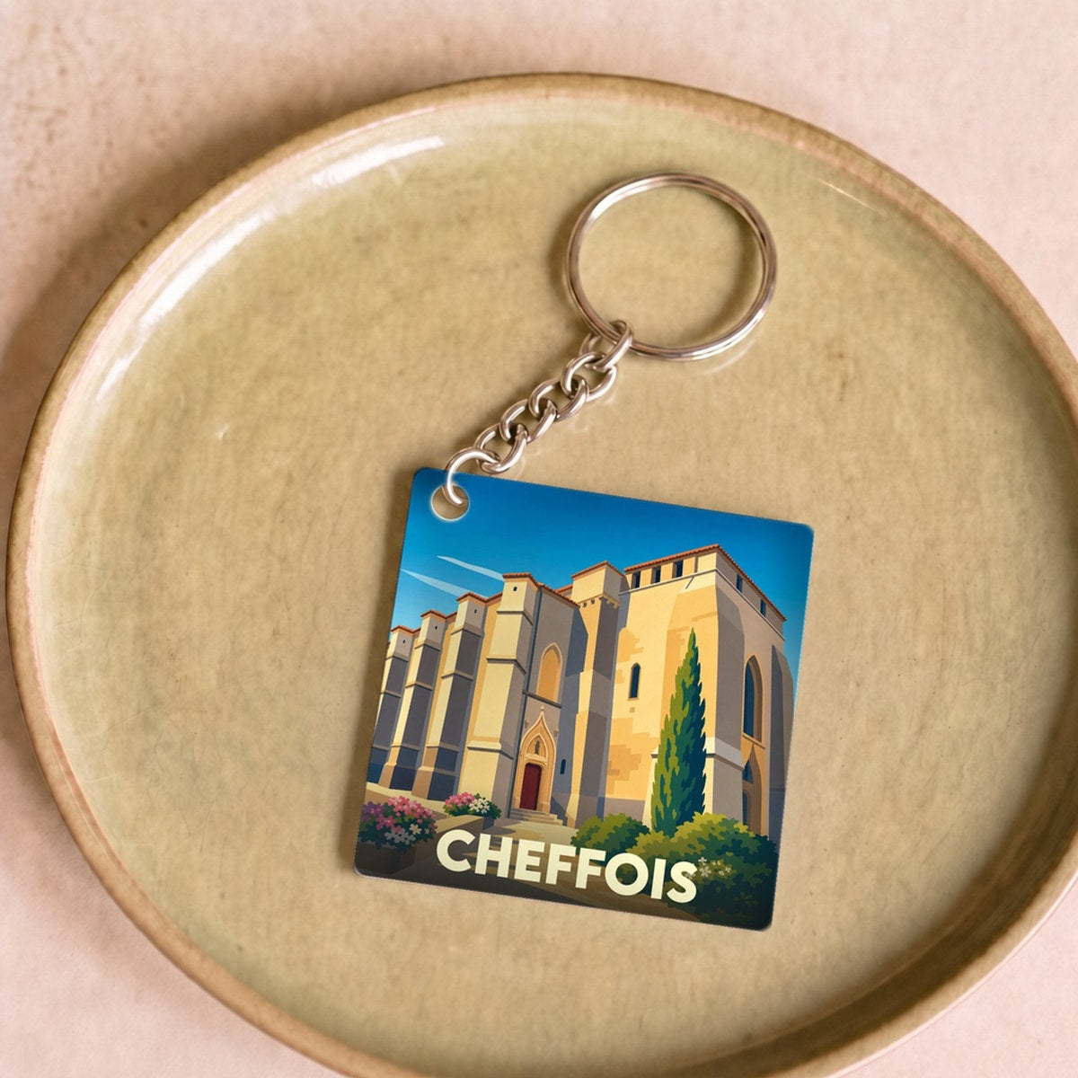 Porte-clés souvenir de la ville de Cheffois avec une illustration stylisée de son église fortifiée.