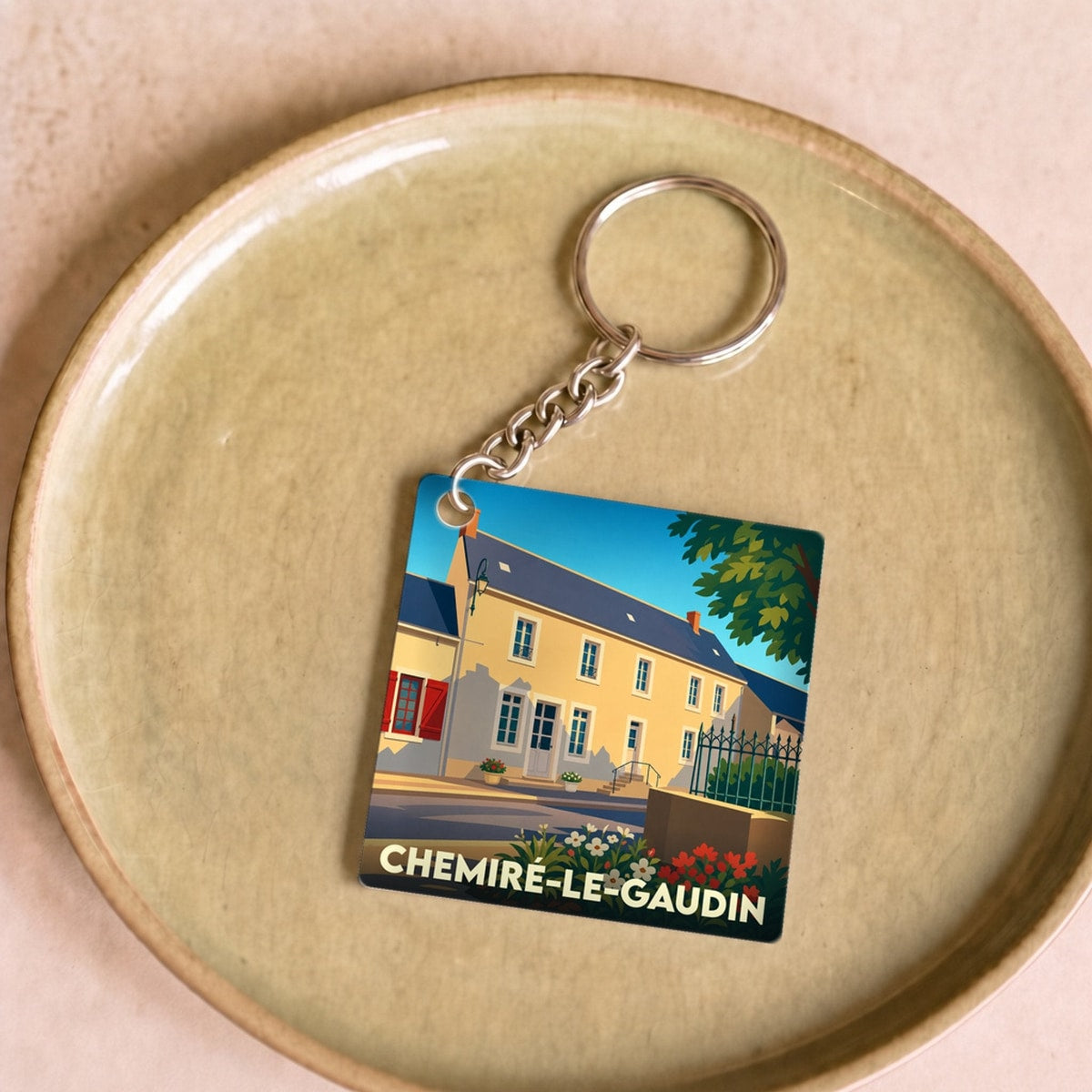 Porte-clés souvenir de la ville de Chemiré-le-Gaudin avec une illustration stylisée d'une maison ancienne.