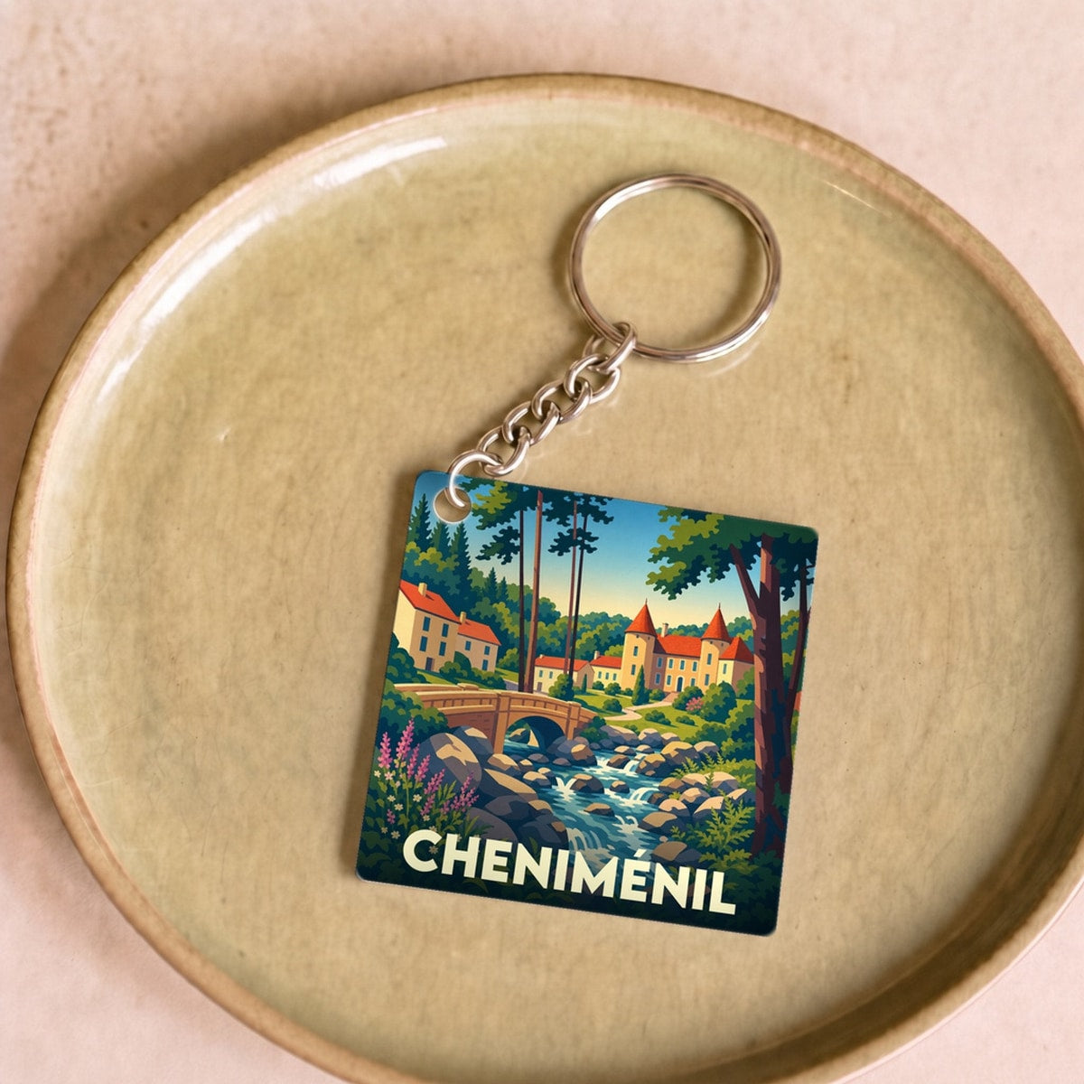 Porte-clés souvenir de la ville de Cheniménil avec une illustration stylisée d'un paysage naturel.