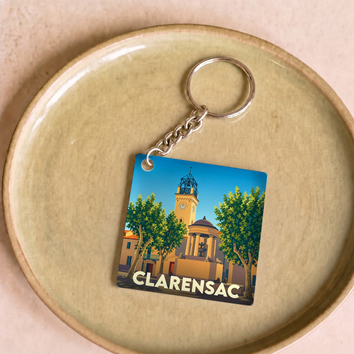 Porte-clés souvenir de la ville de Clarensac avec une illustration stylisée d'une place ensoleillée.
