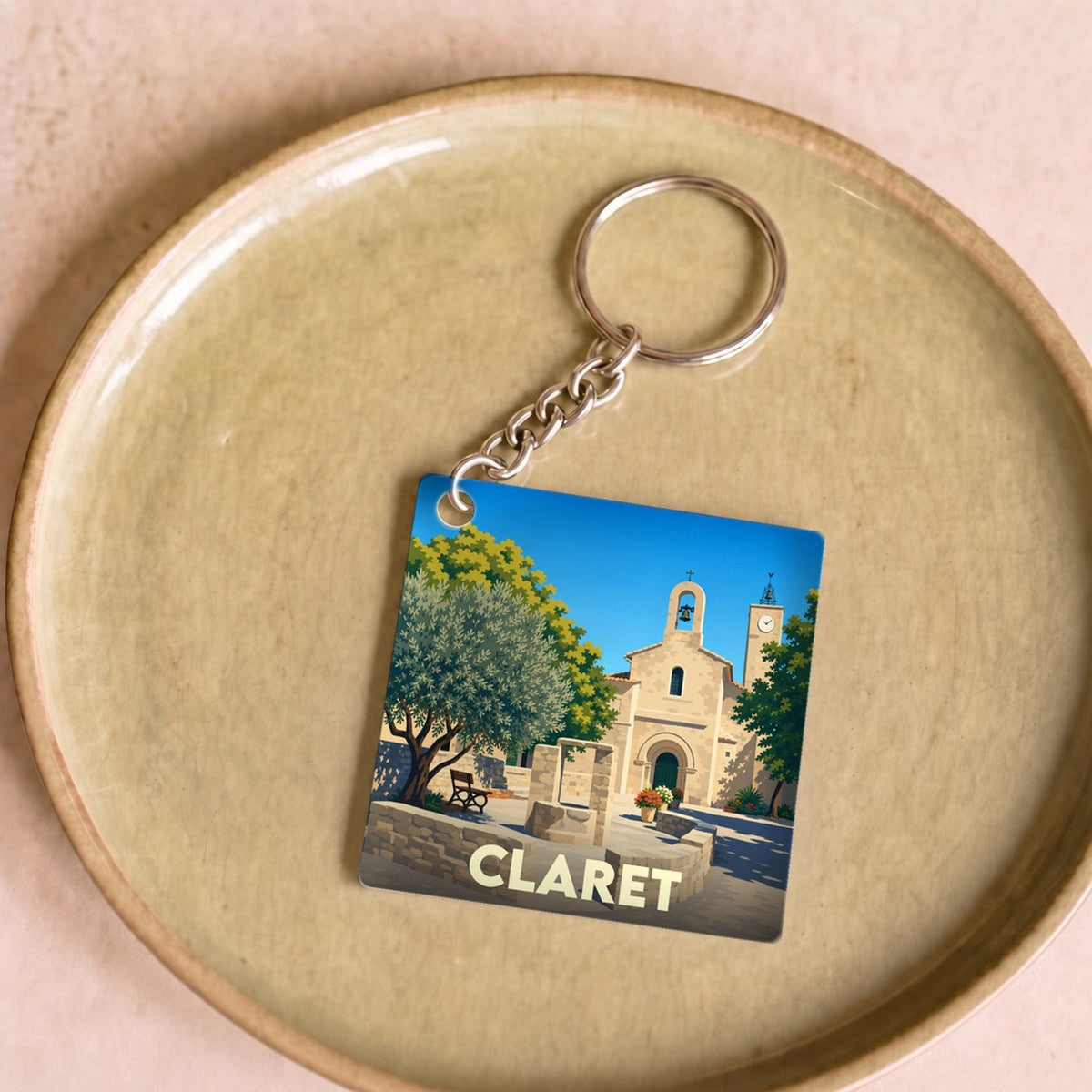 Porte-clés souvenir de la ville de Claret avec une illustration stylisée de son église et de sa place.
