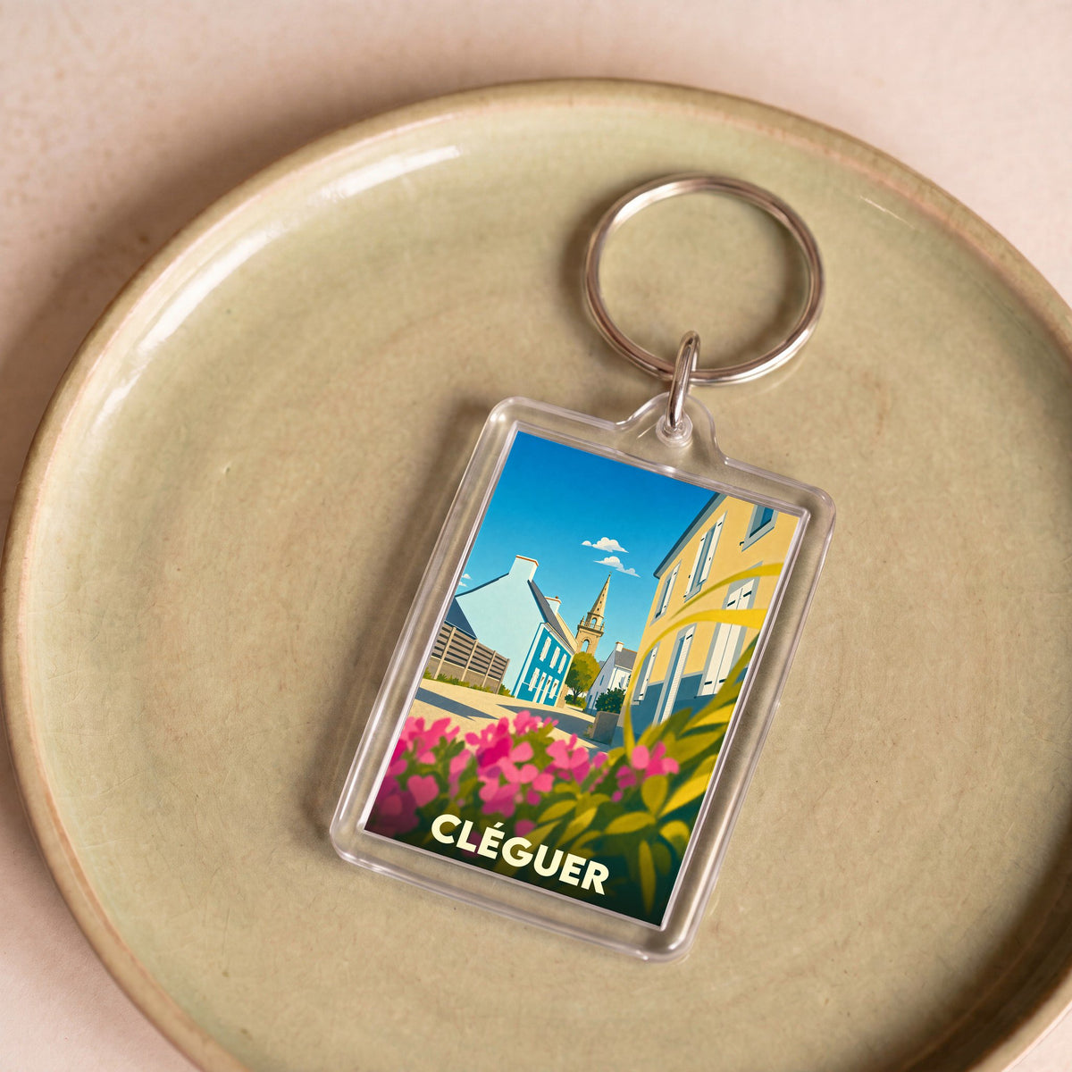 Porte-clés souvenir de la ville de Cléguer avec une illustration stylisée d'une rue fleurie et de son église.
