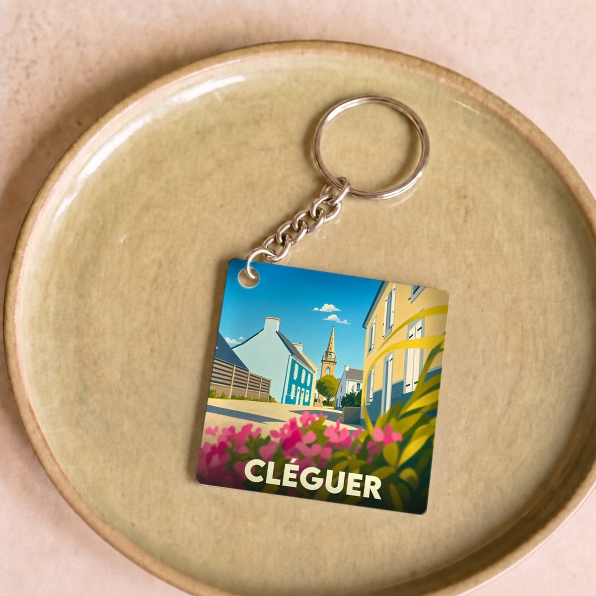 Porte-clés souvenir de la ville de Cléguer avec une illustration stylisée d'une rue fleurie et de son église.