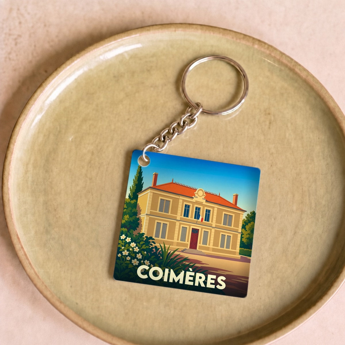 Porte-clés souvenir de la ville de Coimères avec une illustration stylisée d'une bâtisse.
