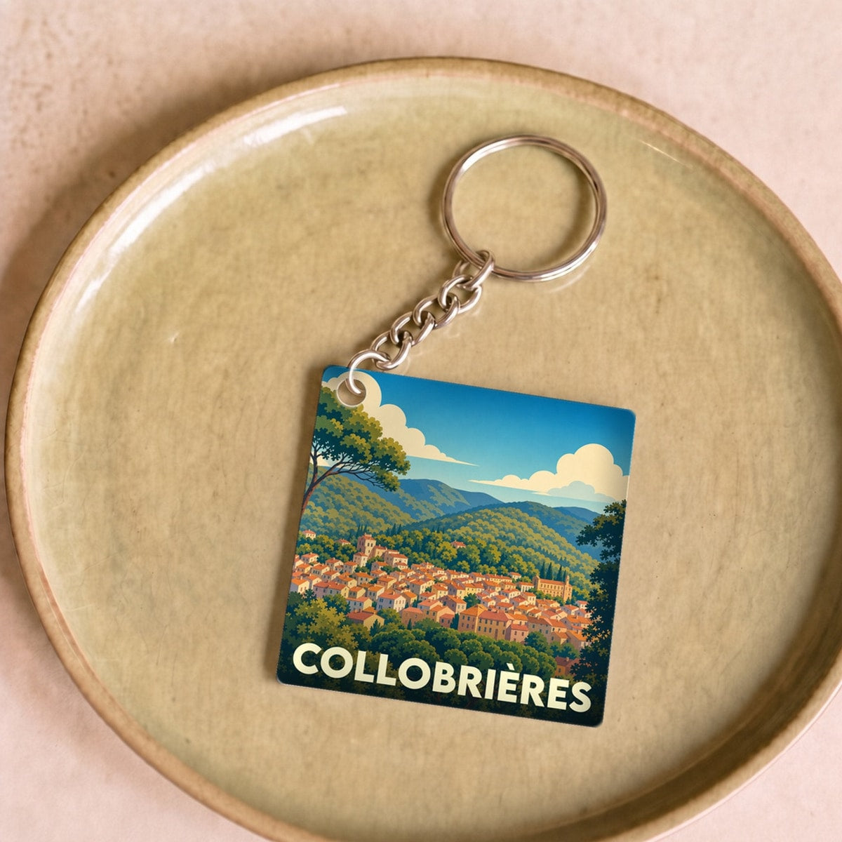Porte-clés souvenir de la ville de Collobrières avec une illustration stylisée de son village niché dans la forêt.