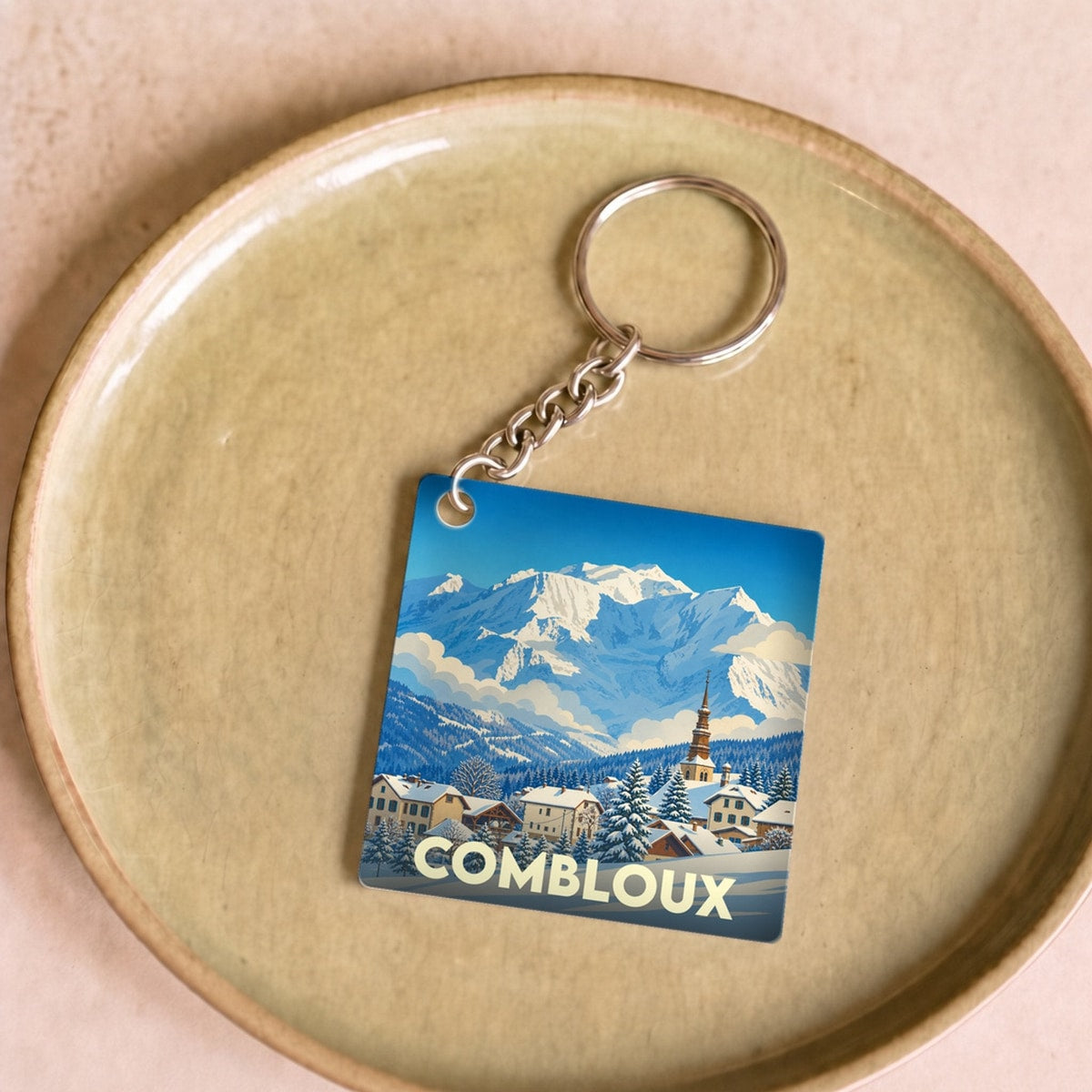 Porte-clés souvenir de la ville de Combloux avec une illustration stylisée de montagne enneigée.