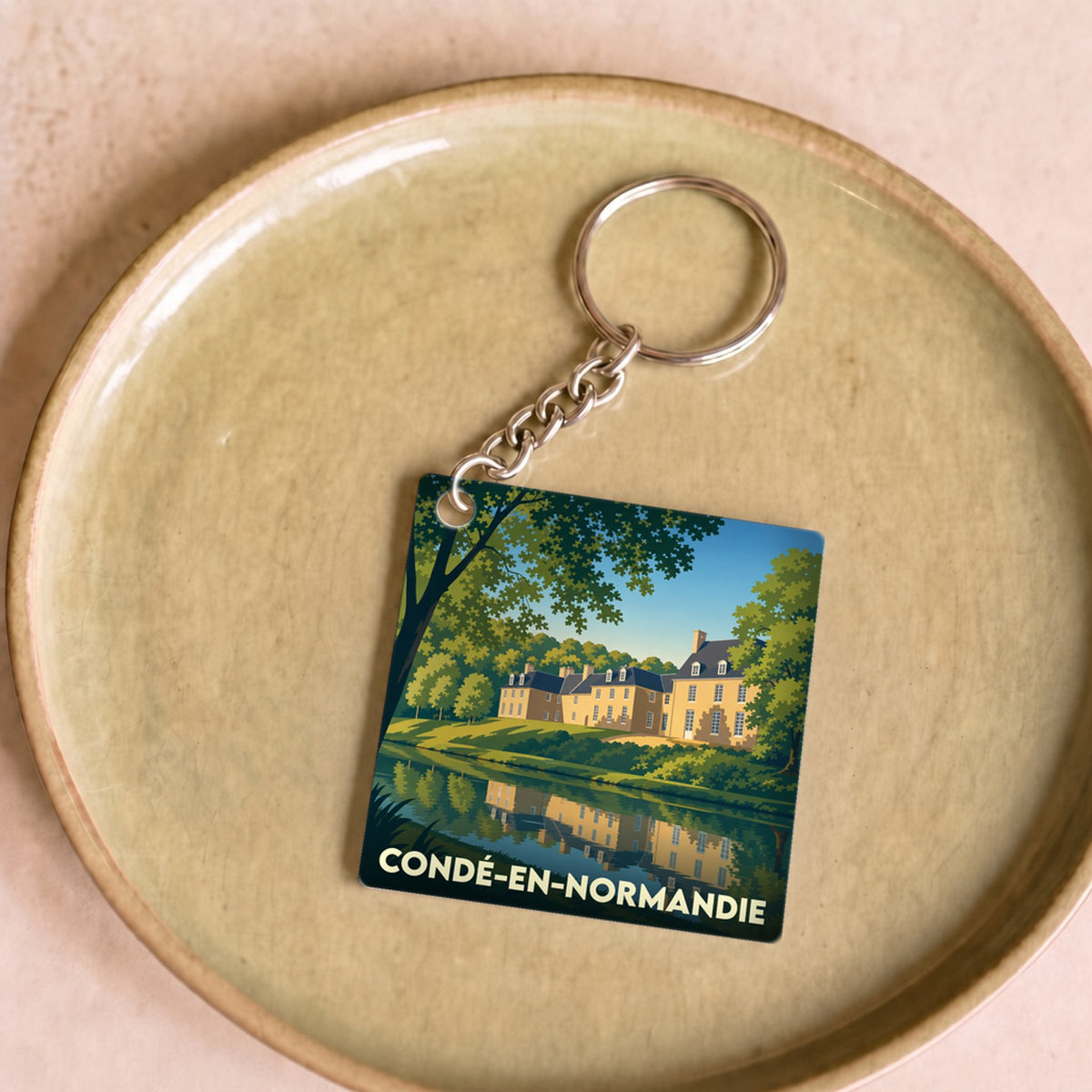 Porte-clés souvenir de la ville de Condé-en-Normandie avec une illustration stylisée d'un manoir se reflétant dans l'eau.