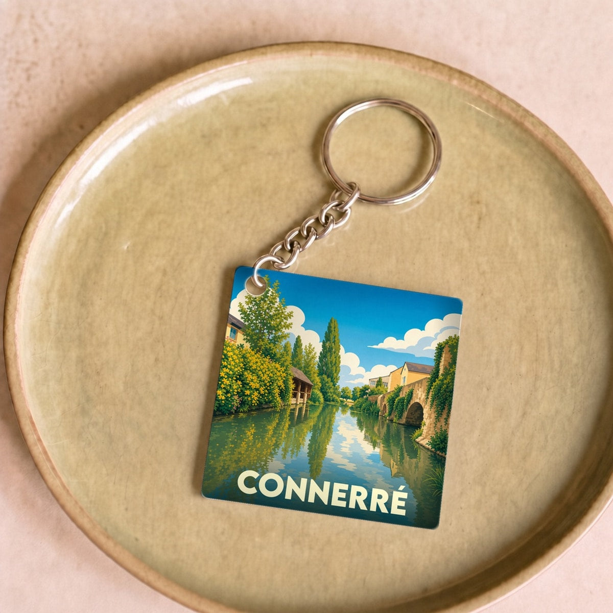 Porte-clés souvenir de la ville de Connerré avec une illustration stylisée d'un paysage de bord de rivière.