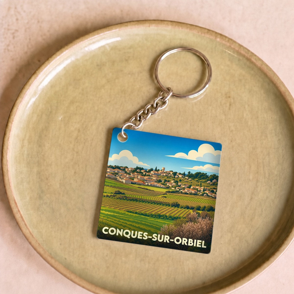 Porte-clés souvenir de la ville de Conques-sur-Orbiel avec une illustration stylisée de ses paysages.
