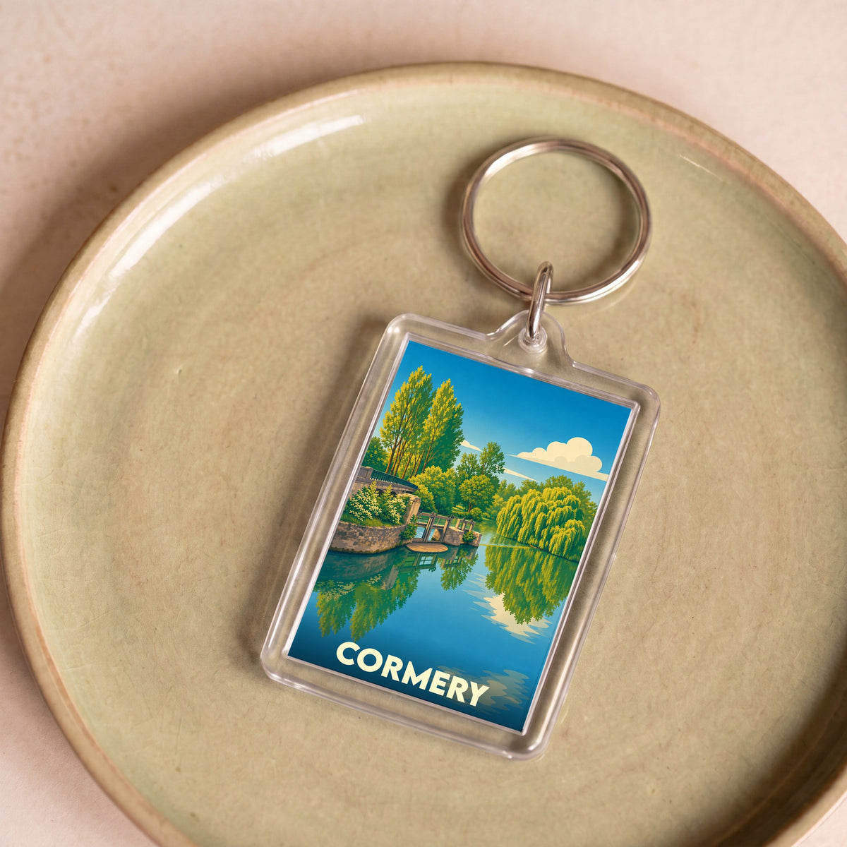 Porte-clés souvenir de la ville de Cormery avec une illustration stylisée d'un paysage de rivière.