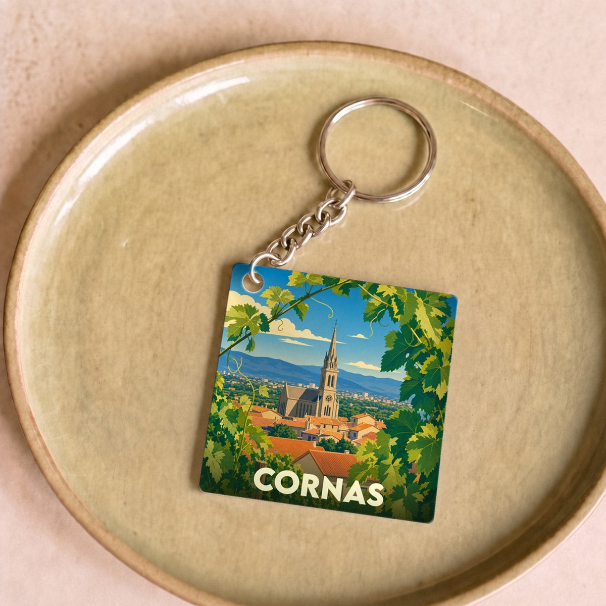 Porte-clés souvenir de la ville de Cornas avec une illustration stylisée de son église entourée de vignes.