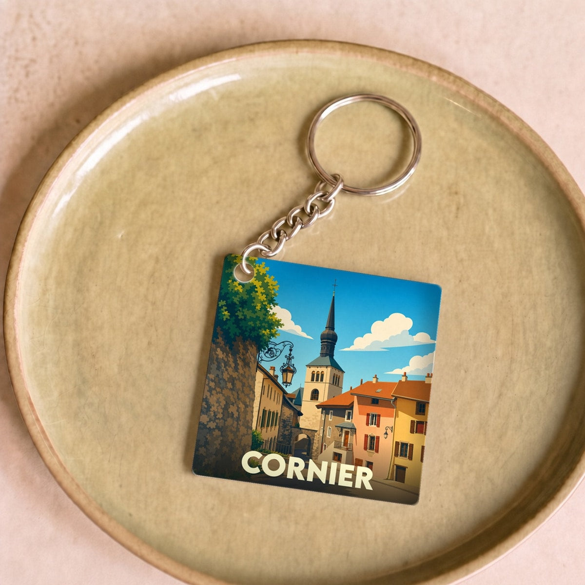 Porte-clés souvenir de la ville de Cornier avec une illustration stylisée d'une rue pittoresque et de son clocher.
