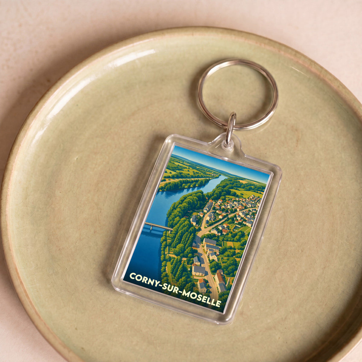Porte-clés souvenir de Corny-sur-Moselle avec une illustration aérienne stylisée de la ville et de la Moselle.