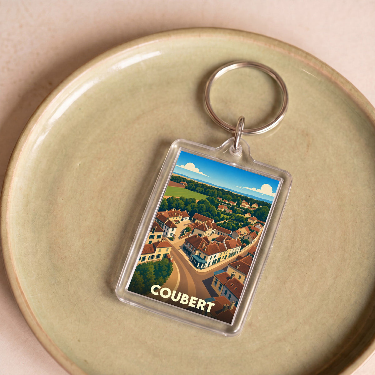 Porte-clés souvenir de la ville de Coubert avec une illustration stylisée d'une vue aérienne du village.