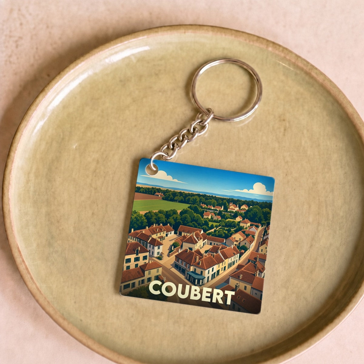 Porte-clés souvenir de la ville de Coubert avec une illustration stylisée d'une vue aérienne du village.