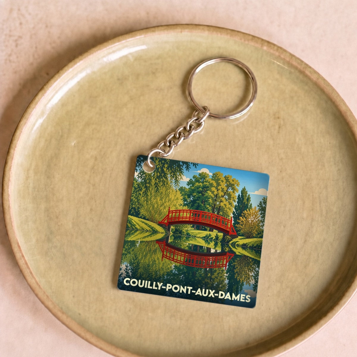Porte-clés souvenir de la ville de Couilly-Pont-aux-Dames avec une illustration stylisée d'un pont rouge se reflétant dans l'eau.