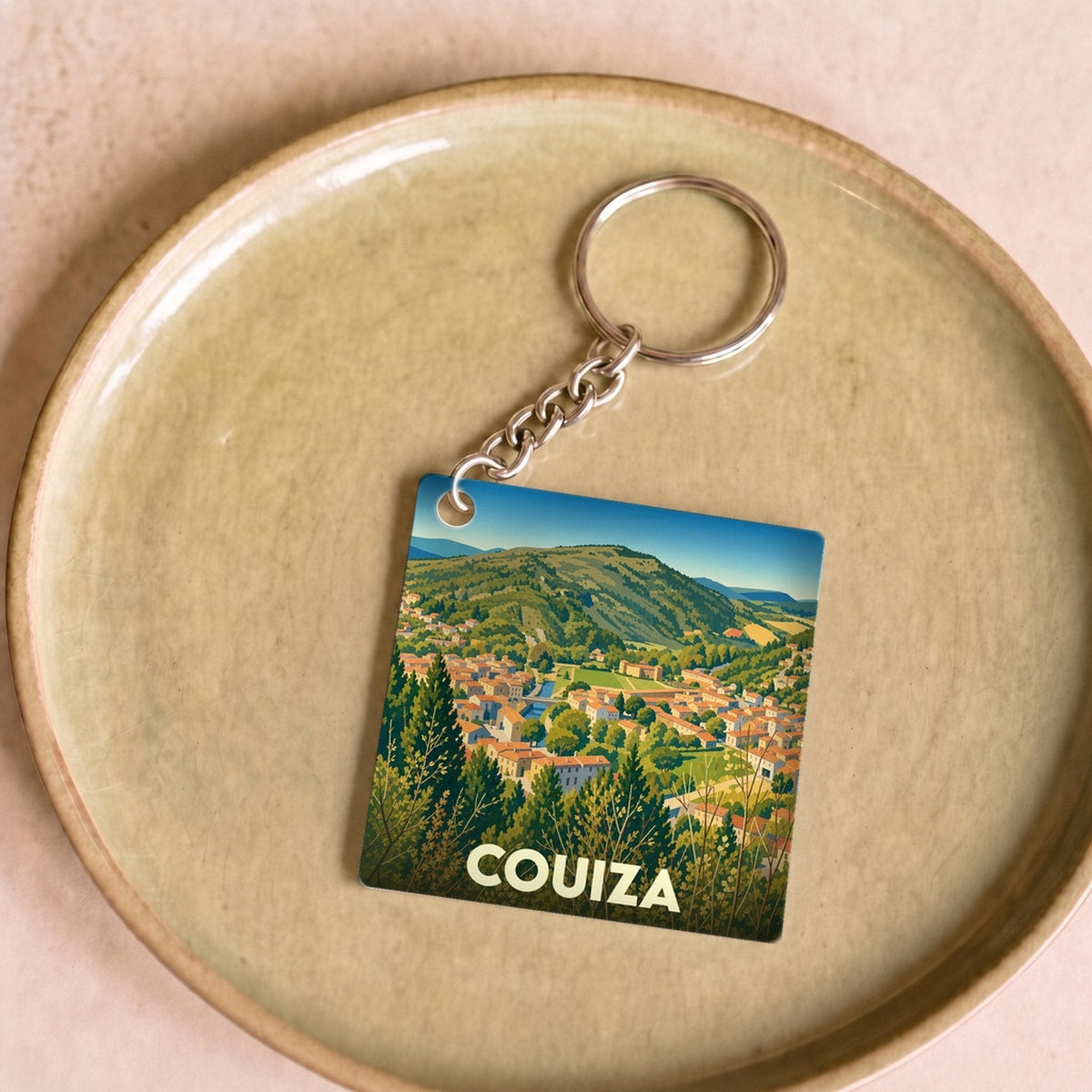 Porte-clés souvenir de la ville de Couiza avec une illustration stylisée d'un paysage de vallée.