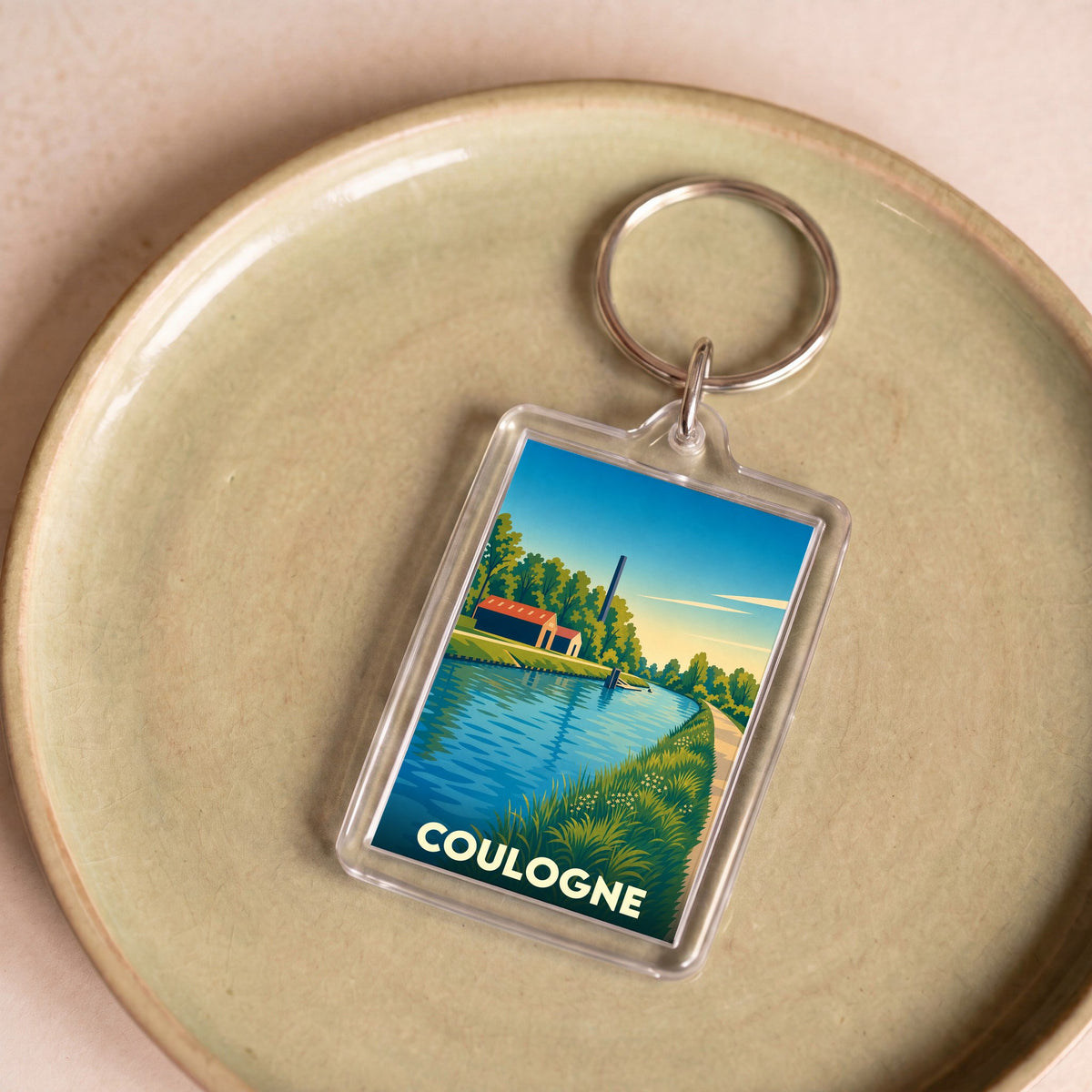 Porte-clés souvenir de la ville de Coulogne avec une illustration stylisée d'un canal et de sa nature environnante.