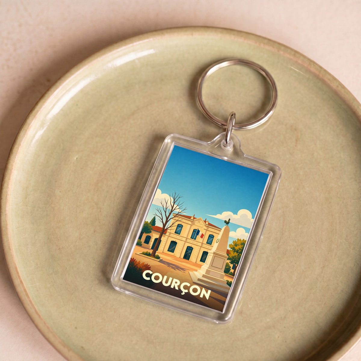 Porte-clés souvenir de la ville de Courçon avec une illustration stylisée de sa mairie et de son monument.