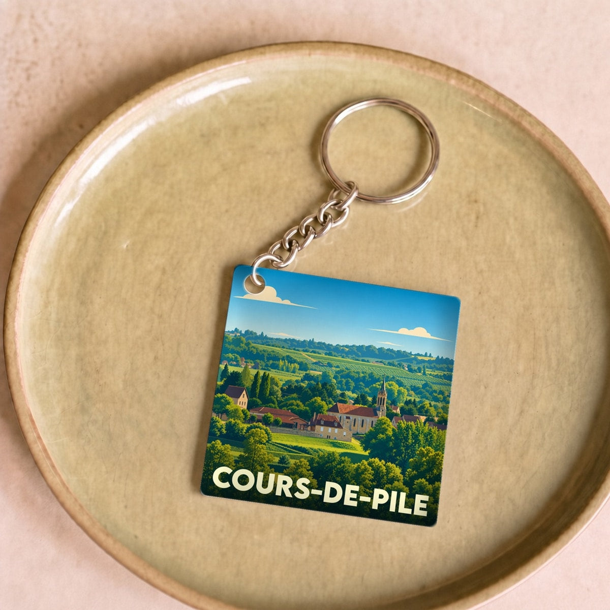 Porte-clés souvenir de la ville de Cours-de-Pile avec une illustration paysagère stylisée.