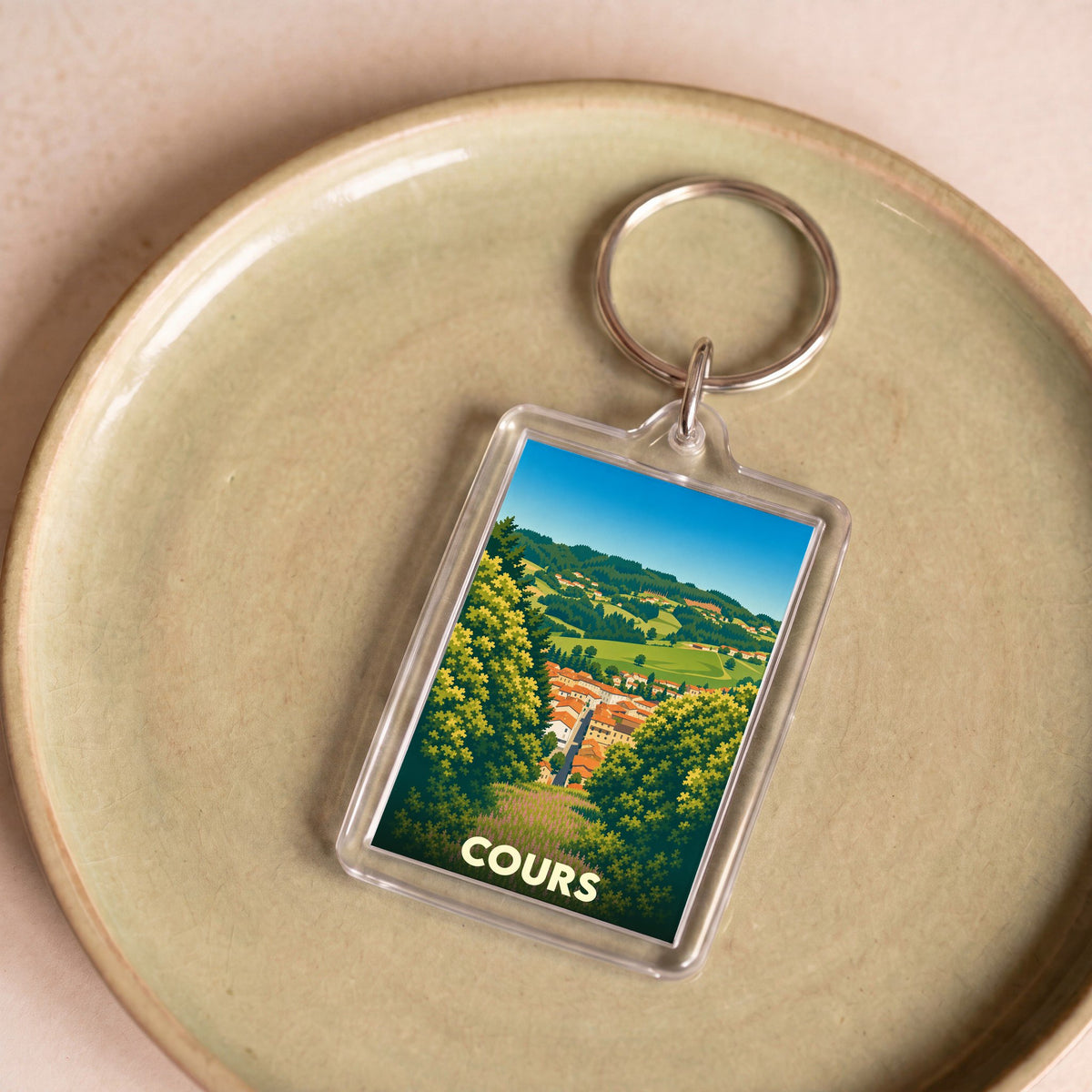 Porte-clés souvenir de la ville de Cours avec une illustration stylisée de son paysage vallonné.