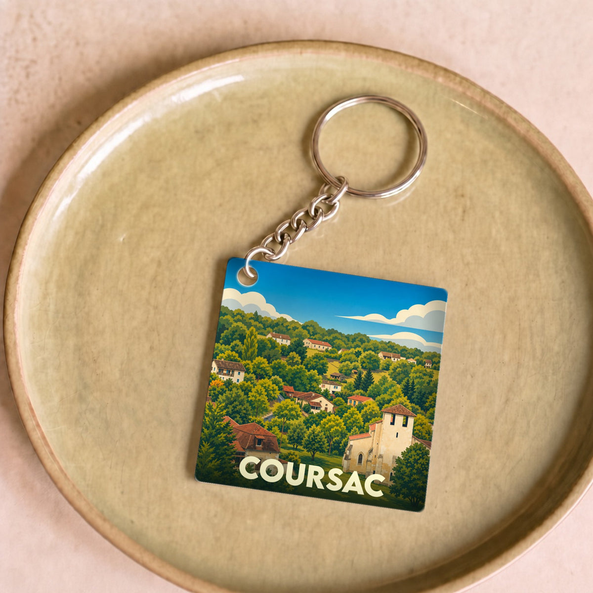 Porte-clés souvenir de la ville de Coursac avec une illustration stylisée de son paysage et de ses maisons.