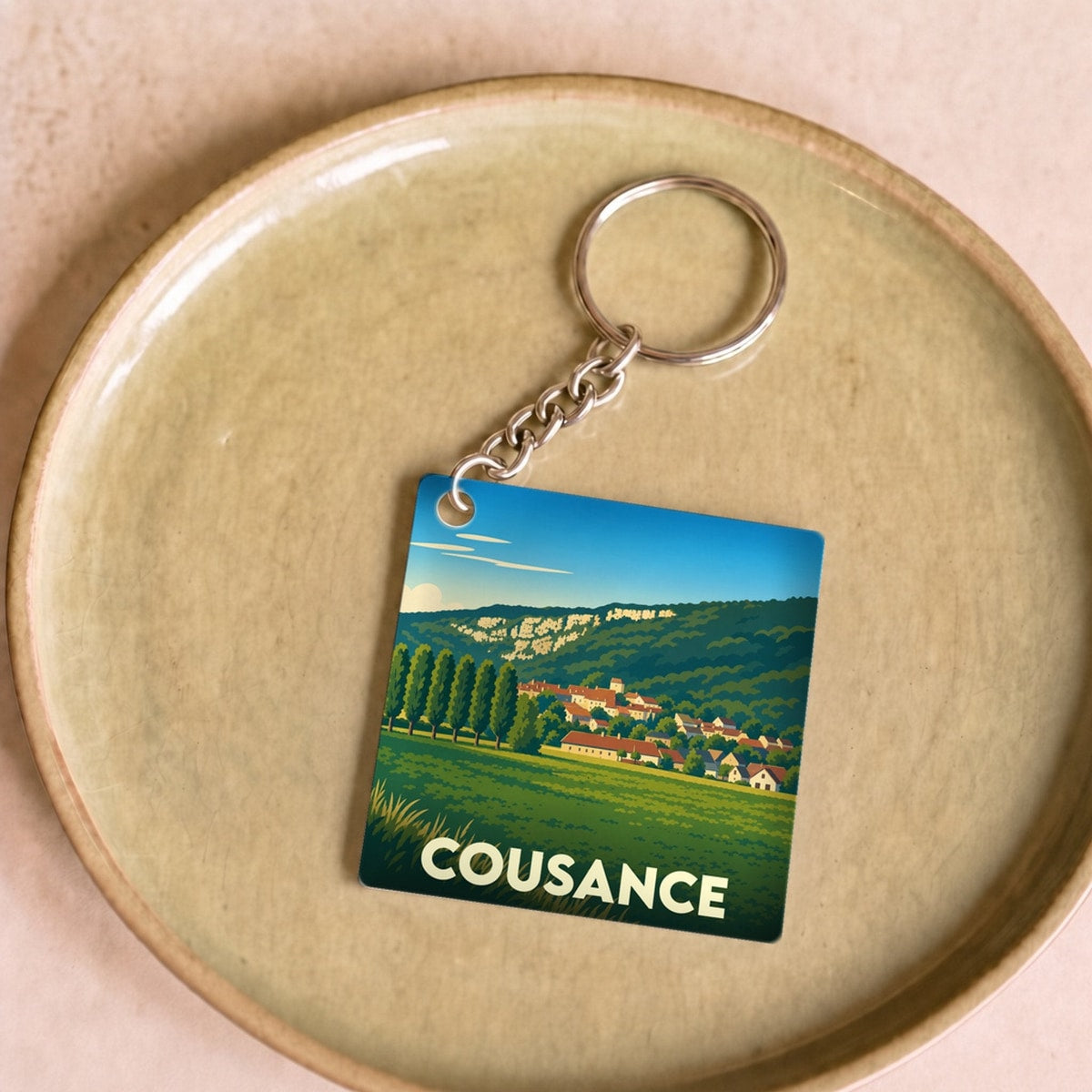 Porte-clés souvenir de la ville de Cousance avec une illustration stylisée de son paysage et de ses habitations.