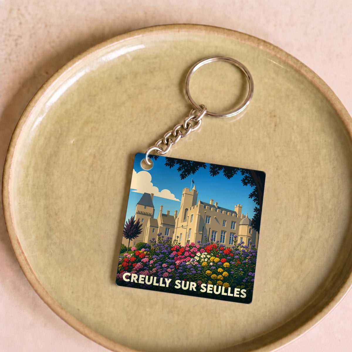Porte-clés souvenir de la ville de Creully sur Seulles avec une illustration stylisée de son château et de jardins fleuris.