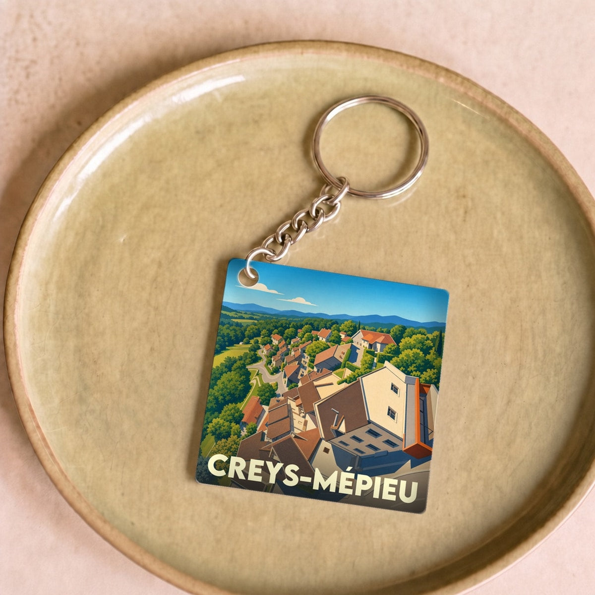 Porte-clés souvenir de la ville de Creys-Mépieu avec une illustration stylisée d'un village.