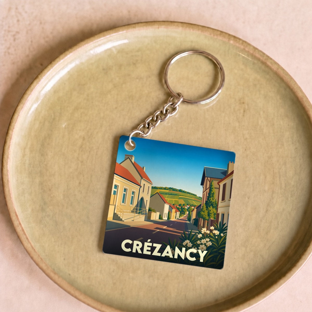 Porte-clés souvenir de la ville de Crézancy avec une illustration stylisée d'une rue ensoleillée.