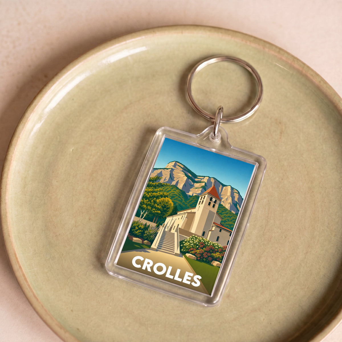 Porte-clés souvenir de la ville de Crolles avec une illustration stylisée de son église et des montagnes.