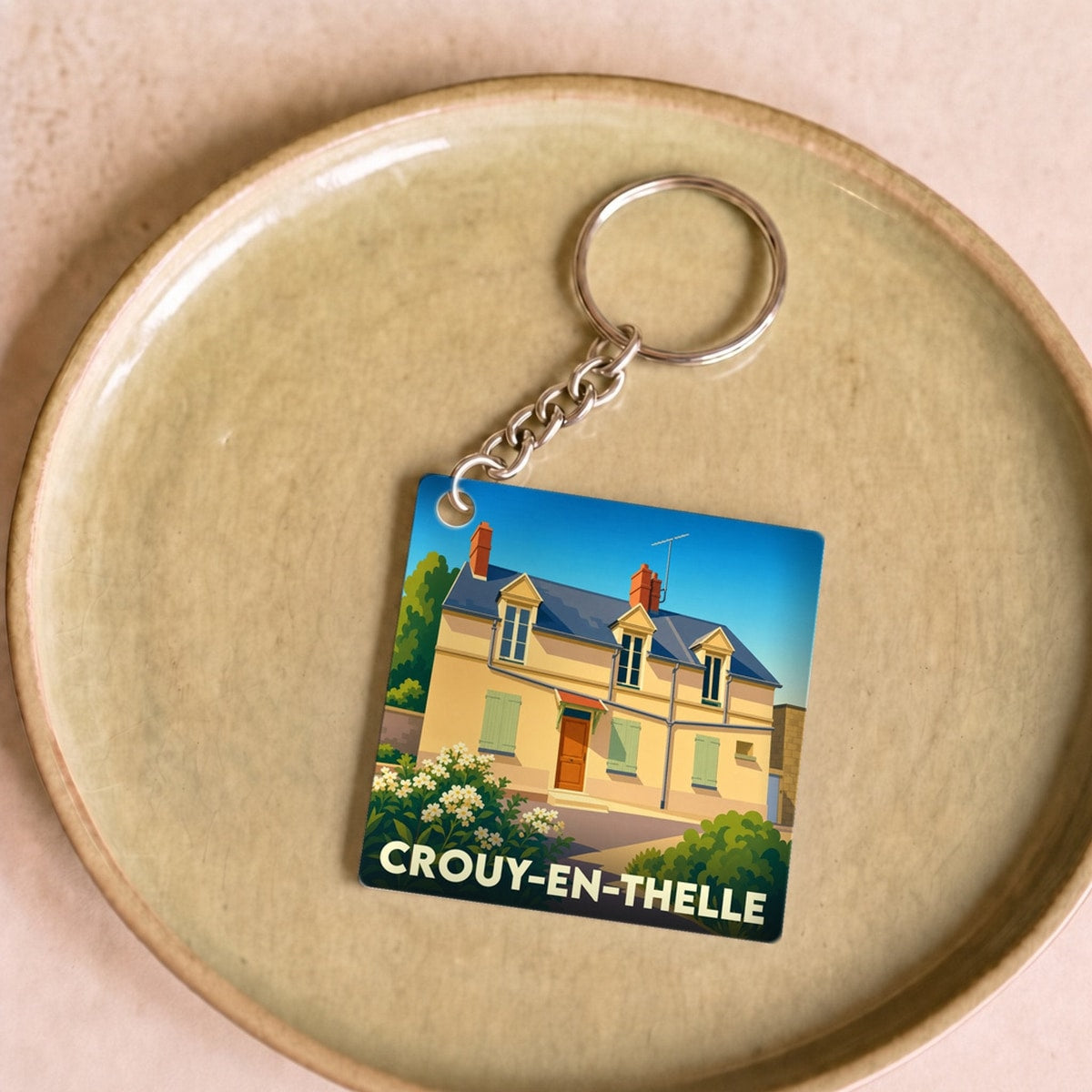 Porte-clés souvenir de la ville de Crouy-en-Thelle avec une illustration stylisée d'une maison traditionnelle.