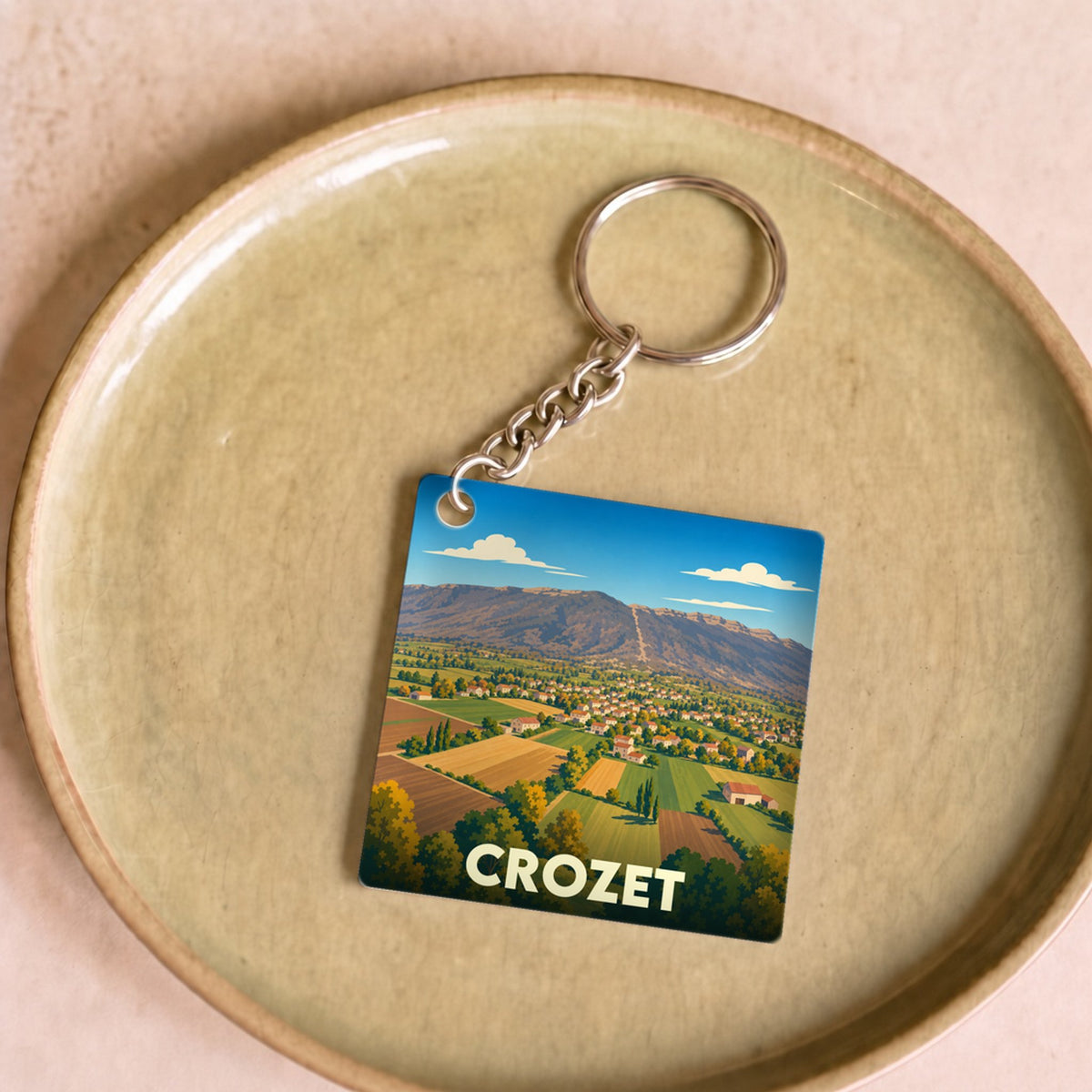 Porte-clés souvenir de la ville de Crozet avec une illustration stylisée d'un paysage montagneux.