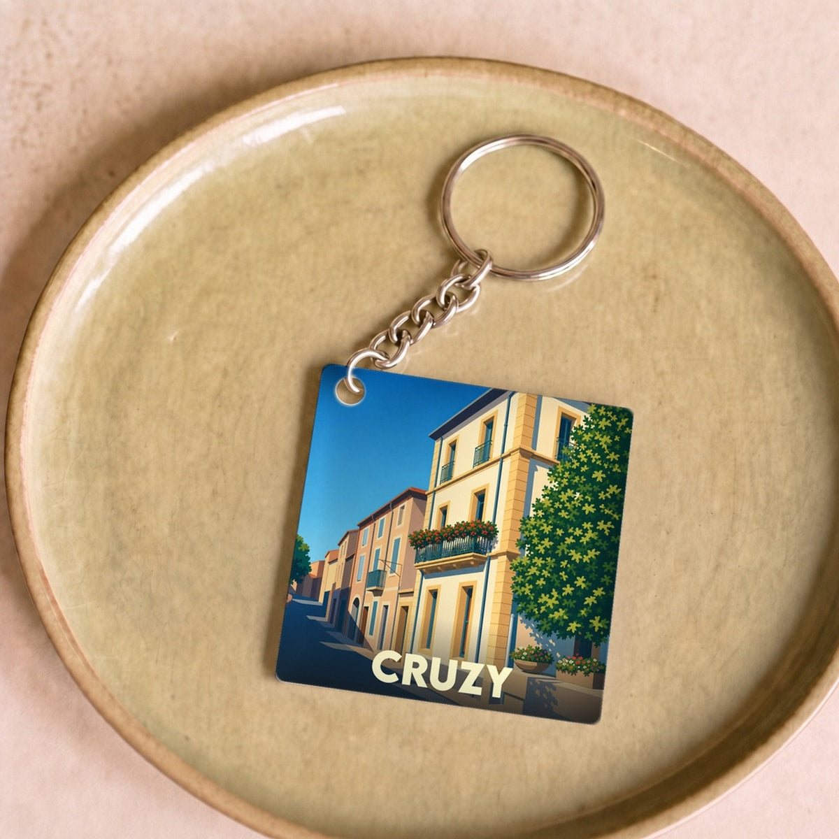 Porte-clés souvenir de la ville de Cruzy avec une illustration stylisée d'une rue ensoleillée.