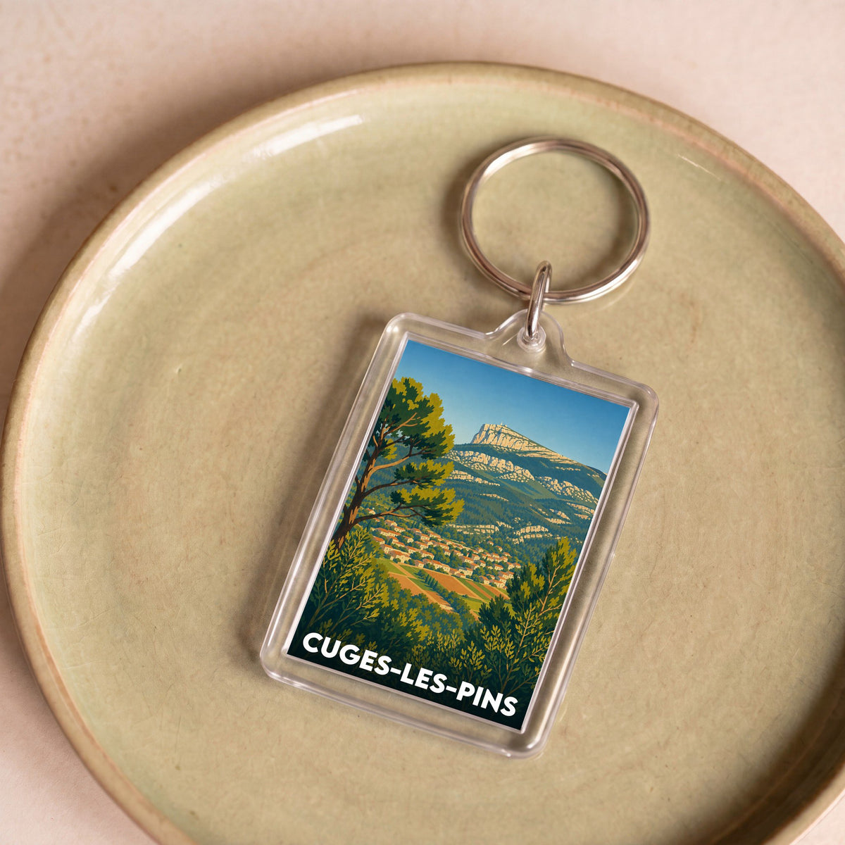 Porte-clés souvenir de la ville de Cuges-les-Pins avec une illustration stylisée d'un paysage provençal.